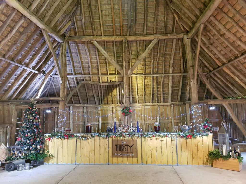 Festive rustic bar setup in a barn with Christmas decorations, fairy lights, and holiday ambiance.