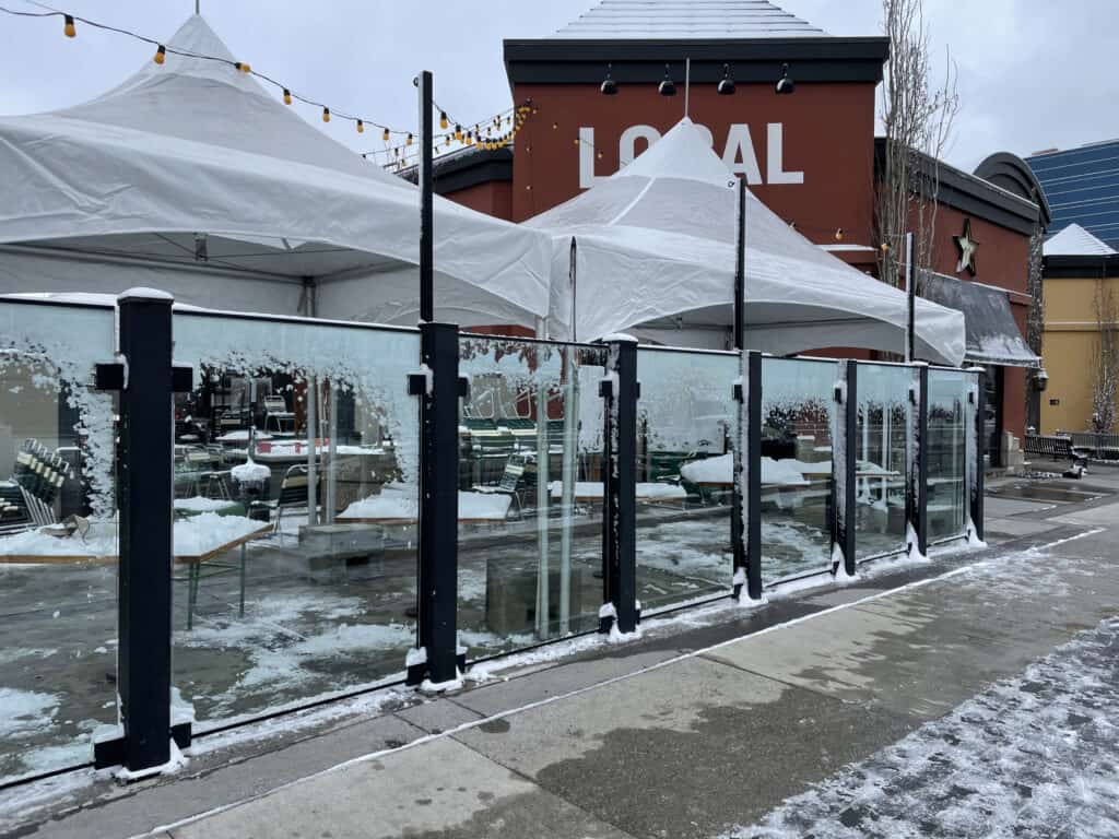 Snow-covered outdoor dining area with glass windbreaks and white tents at Superior Tent Rentals.