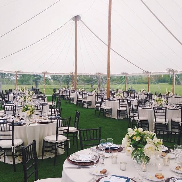 Elegant outdoor wedding tent setup with round tables and floral centerpieces for rent.