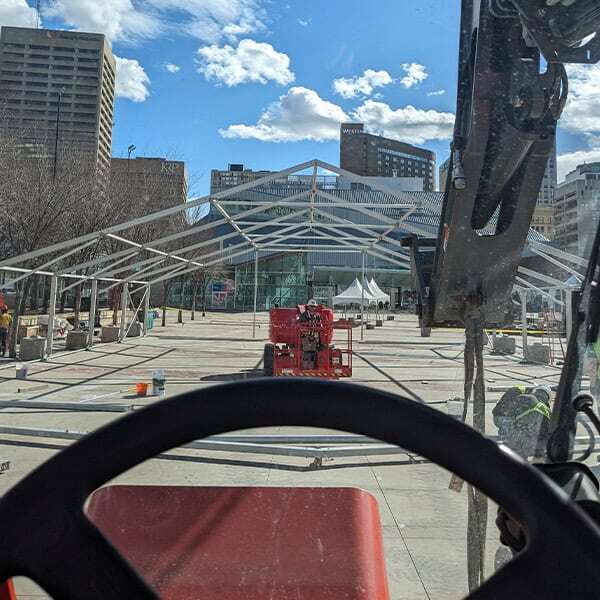 Temporary outdoor event tent structure being assembled by Superior Tent Rentals in an urban setting with high-rise buildings.