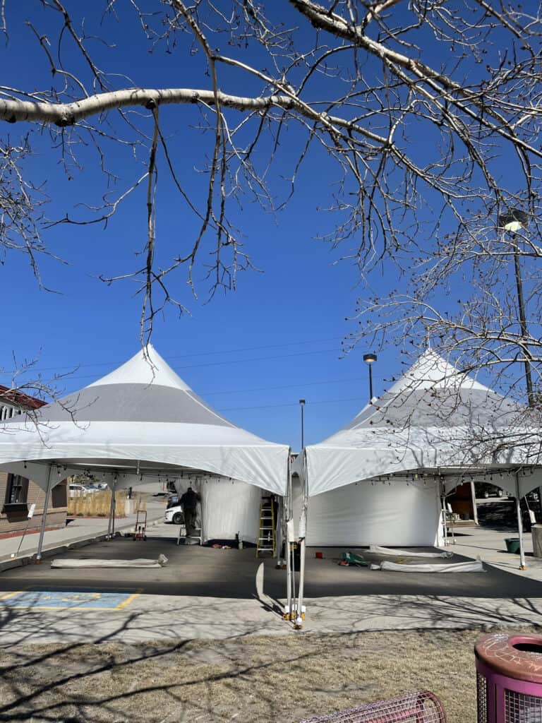 White event tents set up for outdoor celebration or event rental, with clear skies and leafless tree branches overhead.